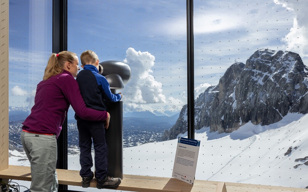 Person mit Kind nutzt ein digitales Fernrohr mit Blick auf den Hallstätter Gletscher.
